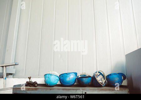 Dirty blue worker helmets on top of an old, rusty and dirty workbench in a workshop Stock Photo
