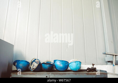 Dirty blue worker helmets on top of an old, rusty and dirty workbench in a workshop Stock Photo