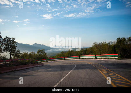 curve road driving a car on mountain road downhill / Dramatic curve beautiful blue sky cloud with mist fog in the morning and forest tree on the roads Stock Photo