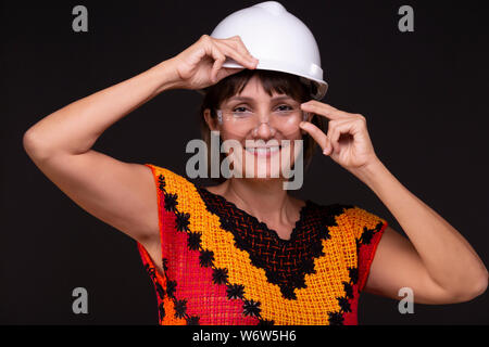 Female engineer or architect with helmet and protective glasses in a colourful hand knitted dress smiling towards the camera. Stock Photo