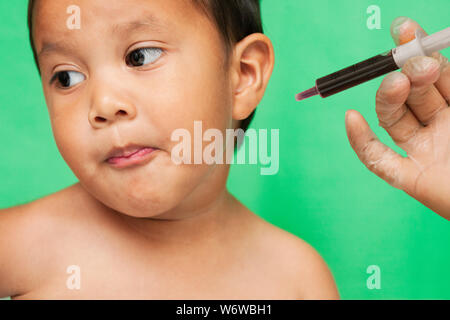 A 3 year old toddler refusing to take oral grape medication for the flu from a medical professional. Stock Photo