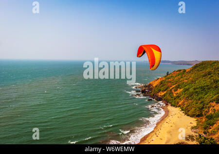 Paragliding in the sky. Paraglider tandem flying over the sea with blue water and mountains in bright sunny day. Aerial view of paraglider and Blue La Stock Photo