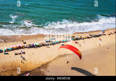 Paragliding in the sky. Paraglider tandem flying over the sea with blue water and mountains in bright sunny day. Aerial view of paraglider and Blue La Stock Photo