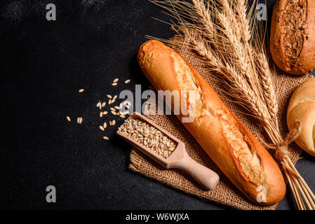 Fresh fragrant bread with grains and cones of wheat against a dark background. Assortment of baked bread on wooden table background Stock Photo