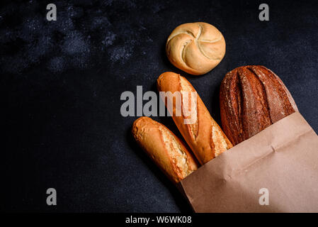 Fresh fragrant bread with grains and cones of wheat against a dark background. Assortment of baked bread on wooden table background Stock Photo