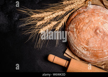 Fresh fragrant bread with grains and cones of wheat against a dark background. Assortment of baked bread on wooden table background Stock Photo