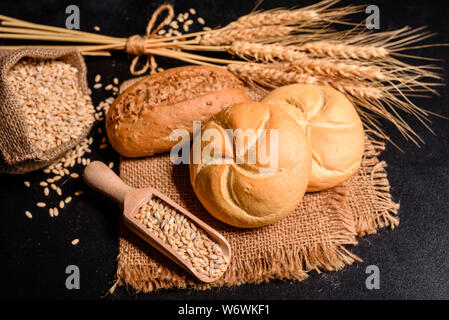 Fresh fragrant bread with grains and cones of wheat against a dark background. Assortment of baked bread on wooden table background Stock Photo