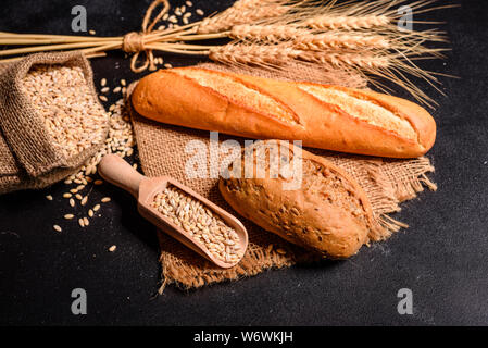 Fresh fragrant bread with grains and cones of wheat against a dark background. Assortment of baked bread on wooden table background