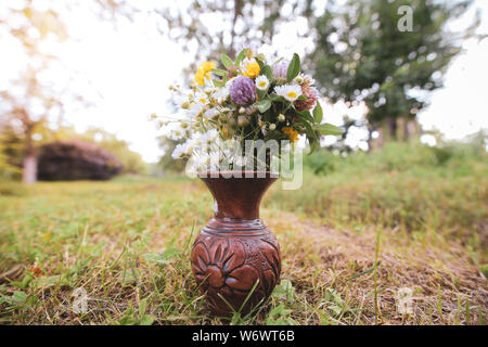 Bouquet of colorful wild wild flowers in a broken clay pot laid on the grass Stock Photo