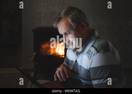 man watching content on a laptop in the evening at home by the fireplace Stock Photo