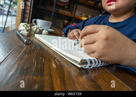 Asian female student drawing on blank sketchbook beside crumpled papers Stock Photo
