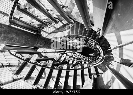 Looking down from the top of a circular staircase; bright light passing through the glass panels of the railing and creating shadows and shapes on the Stock Photo