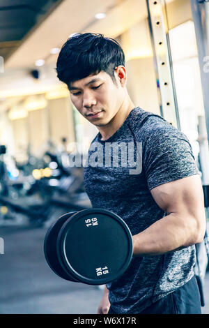 Young Asian man working out lifting heavy dumbbell at a fitness gym, healthy lifestyle Stock Photo