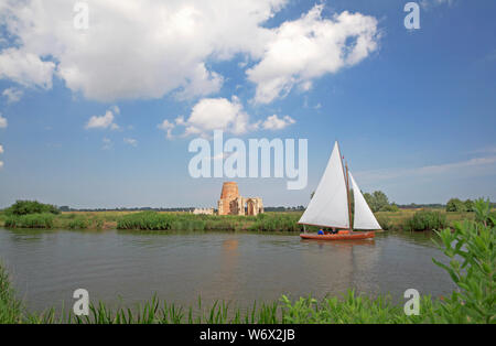 A yacht in full sail on the River Bure on the Norfolk Broads passing St Benet's Abbey and viewed from South Walsham, Norfolk, England, UK, Europe.