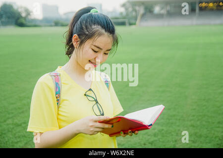 Young girl student reads a book on grass field in the afternoon in campus Stock Photo