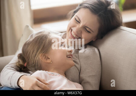 Preschool daughter and cheerful mother lying on couch joking laughing Stock Photo