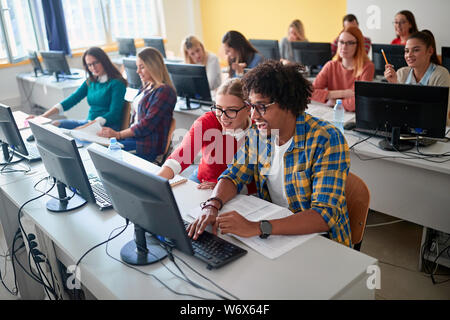 Smiling students sitting together at table using computer in class. Stock Photo