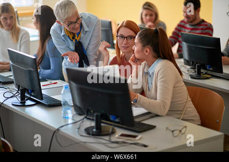 lecturer with smiling girl students working in computer class on university campus Stock Photo