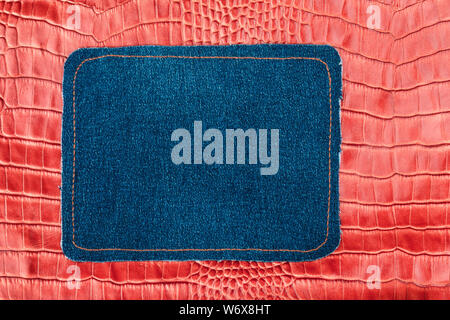 Blank jeans frame. Denim patch with orange thread seam on red skin. With space for design, text place. Stock Photo