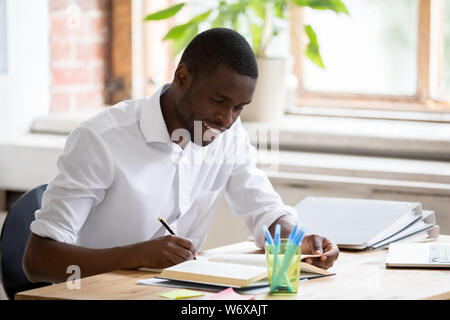 Smiling african student holding pen making notes preparing for test Stock Photo