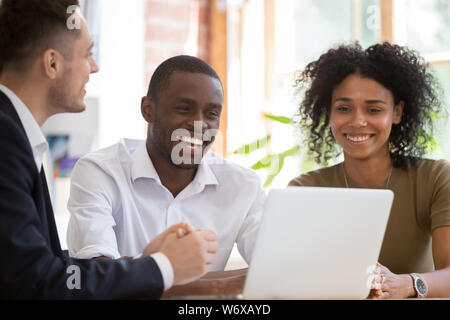 Cheerful diverse colleagues partners working using computer sitting at desk Stock Photo