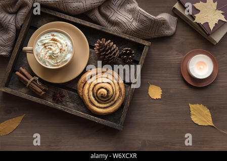 Cozy home and autumn hygge concept. Seasonal autumnal composition with soft plaid, coffee latte, fresh pastry cinnamon bun, candle on wooden, top view Stock Photo