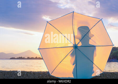 Stylish hipster. SILHOUETTE CLOSE UP: Kid in hat hides behind umbrella Silhouette of a man back view on sunset sunrise background, the effect of backlight, darkened picture. Copy space Stock Photo