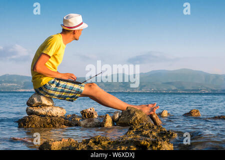 Young hipster using laptop computer, concept of tourist. Man working on laptop computer in tropical exotic ocean. Internet connection 3G, 4G. Virtual office. Travel and work. Male works on seashore Stock Photo