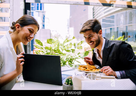 Discussing business. Two cheerful business people in casual wear smiling and using laptop in coffee bar Stock Photo