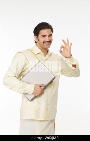 South Indian man holding a laptop and showing OK sign Stock Photo
