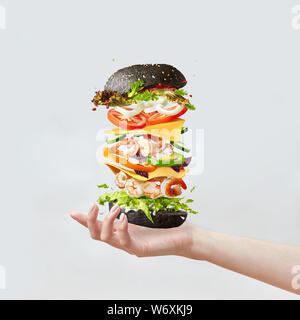 Fresh homemade burger from natural organic ingredients shrimp and vegetables above the female's hand on a light grey background with copy space. Stock Photo