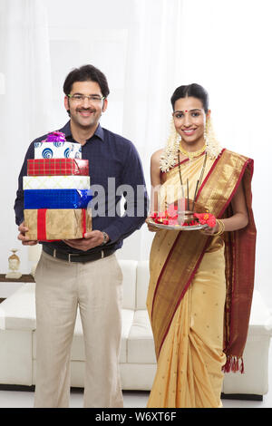 South Indian man holding gift boxes with his wife standing with pooja thali Stock Photo