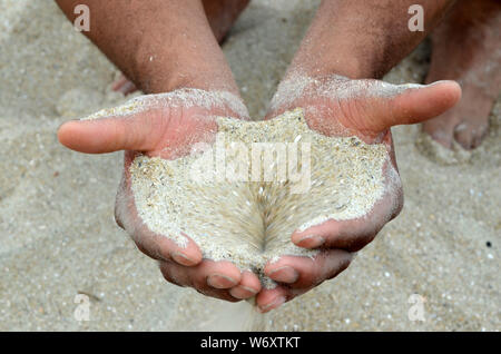 DNA Human: A man and woman squatting on Tybee beach have sand pouring through their hands. Stock Photo
