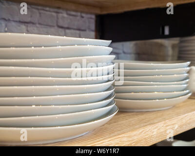 Stack of porcelain plates stacked in two piles on kitchen shelf Stock Photo