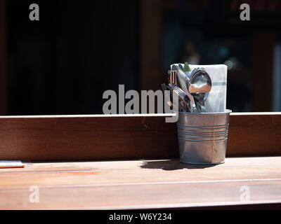 Utensils and napkin sitting in silver bucket on wooden table Stock Photo