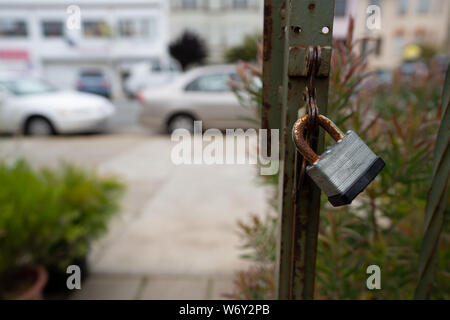 Rusted lock on outdoor gate leading to sidewalk in urban area Stock Photo