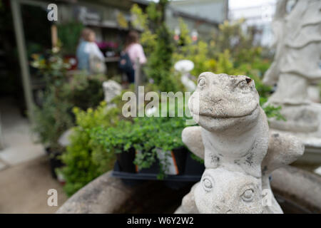 Stone frog sculpture in garden area with women walking background Stock Photo