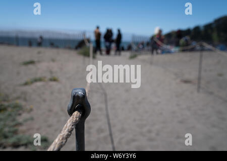 Wire fence on rail on beachside leading to ocean with tourist Stock Photo
