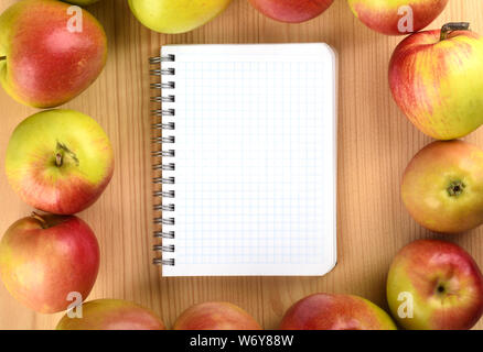 Close up notepad. Squared paper notebook on wooden table top view. Ripe apples around the notebook. Stock Photo