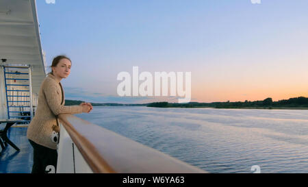 Woman admiring landscape from deck of cruise ship after sunset