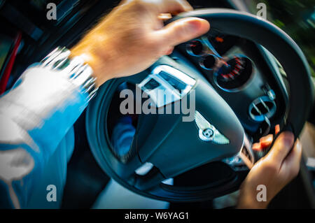 mans hands on a moving Bentley Continental GTC Supersport car steering wheel Stock Photo