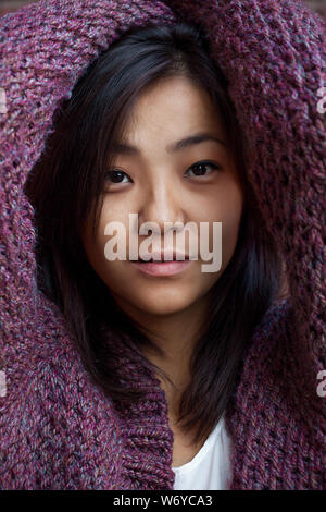 beautiful Asian young woman is in purple knitted cardigan near brick wall Stock Photo