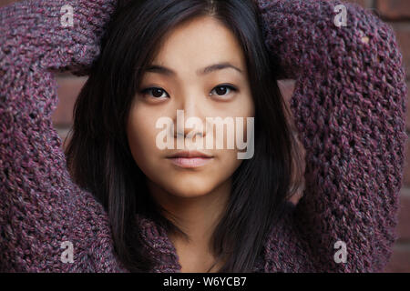 beautiful Asian young woman is in purple knitted cardigan near brick wall Stock Photo