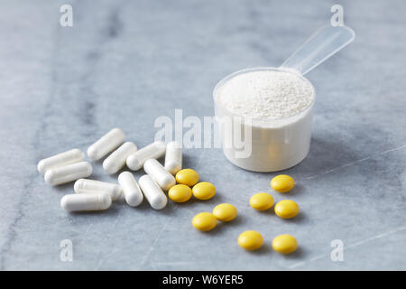 Collagen powder, Proline capsules and Vitamin C tablets. Supplements to support collagen production. Bright stone background. Close up. Stock Photo