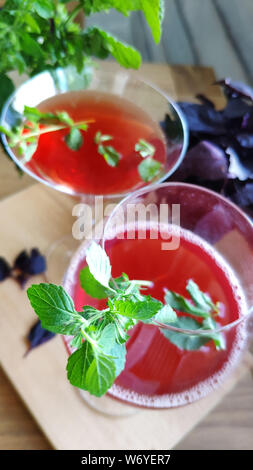 Top view of two glasses with a red refreshing cocktail decorated with mint leaves on a background of bunches of mint and purple basil, selective focus Stock Photo