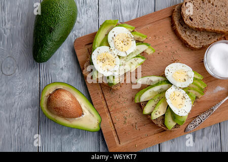 two sliced tasty avocado sandwiches with egg and spices on a wooden Board. Top view Stock Photo