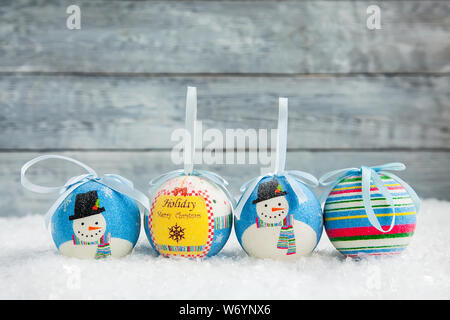 four Christmas blue balls with a snowman pattern on a snowy wooden background Stock Photo