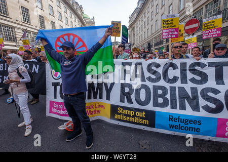 London, UK. 3rd August 2019. A man holds up the Romani flag in front of the Stand Up to Racism banner on the march in London to stop the racist 'Free Tommy' protesters marching. They say Tommy Robinson, in prison for deliberate contempt of court, is part of a far-right movement spreading violence across the world, whipping up hatred against Muslims and refugees. The Anti-fascists set off up Regent St and the Anti-racists joined behind them. Police stopped them close to Oxford Circus, but they went through side streets to get close to the 'Free Tommy' event before being stopped again. Peter Mar Stock Photo