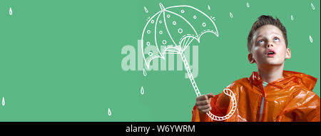 a boy in an orange raincoat and with a painted umbrella stands in the rain Stock Photo