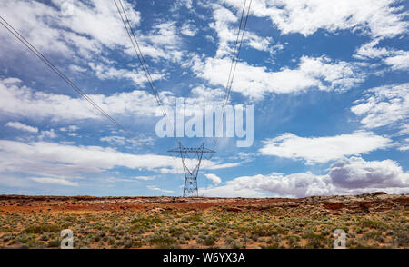 Electricity pylon, high voltage power transmission in the desert, USA. Blue cloudy sky, red rocks landscape, sunny spring day
